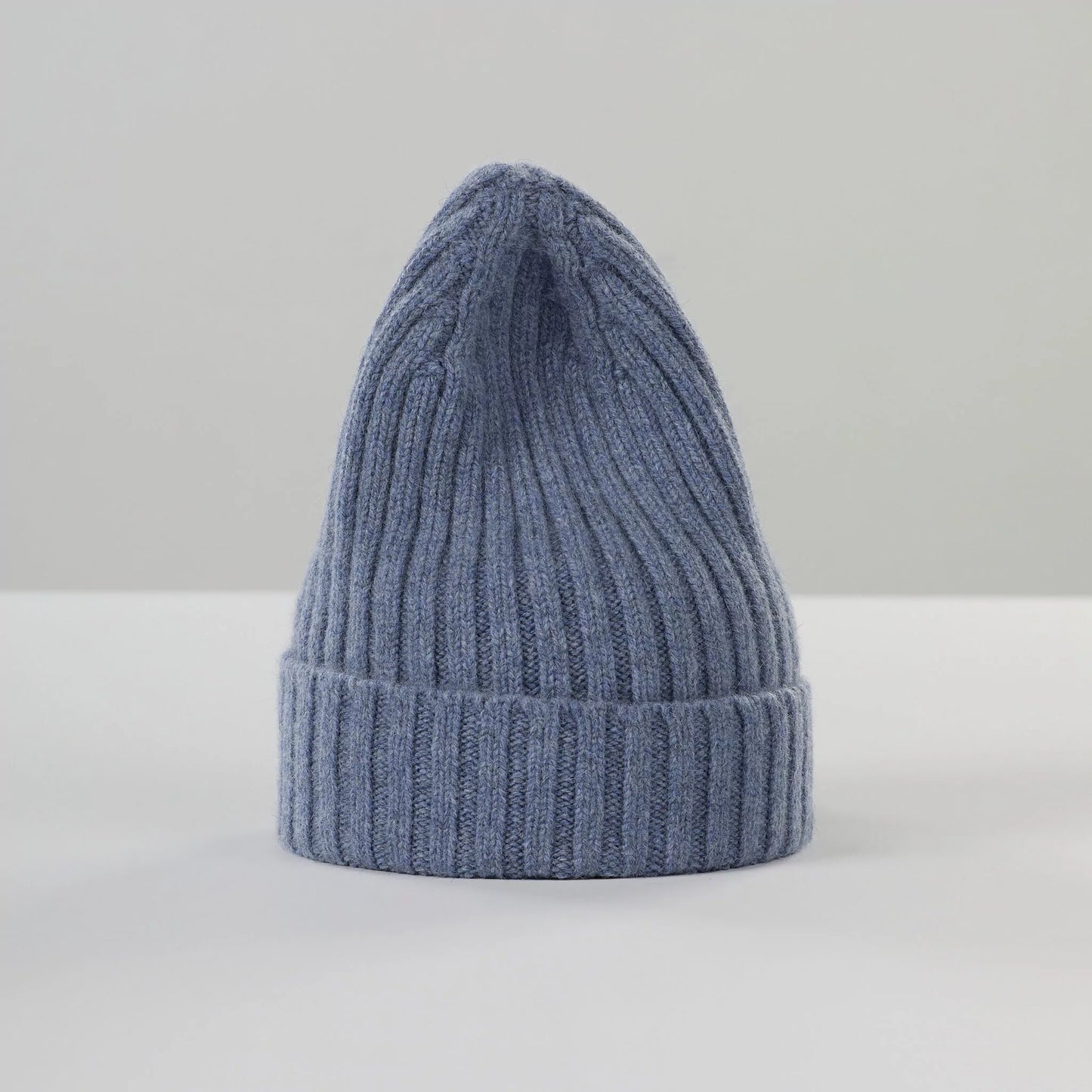 A Le Bonnet Large Beanie in Washed Denim sits on a white surface against a plain background, highlighting its cozy knit and sustainable, biodegradable materials.