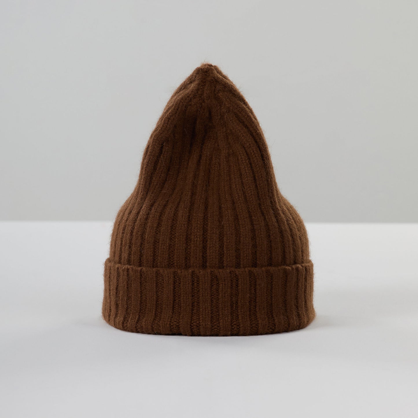 The Large Beanie, Walnut by Le Bonnet, a brown ribbed knit with a pointed tip, is flatly displayed against a plain backdrop, providing extreme comfort and stylish warmth.