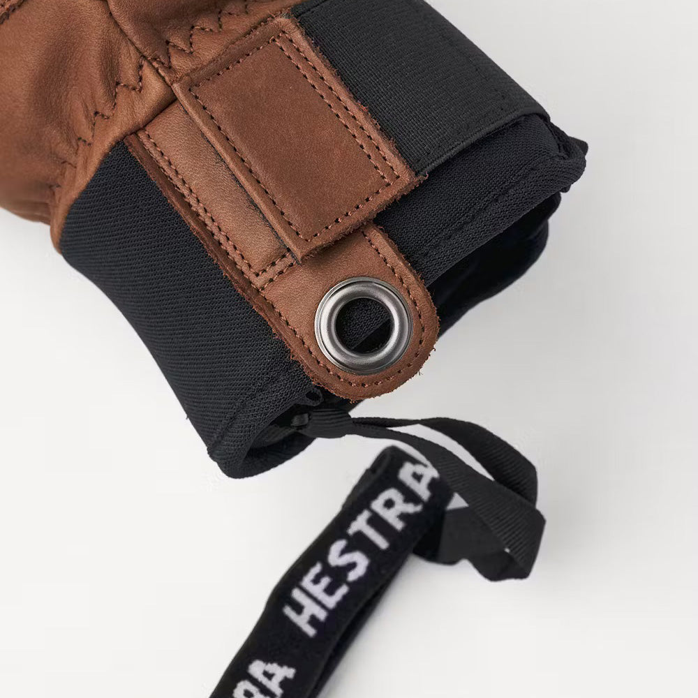 Close-up of the Hestra Fall Line Glove in brown, crafted from durable cowhide and featuring a metal eyelet with a "Hestra" labeled strap.