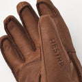 The Fall Line Glove in brown, by Hestra, is crafted from durable cowhide leather with visible stitching and "HESTRA" on the index finger. Enhanced with foam insulation, these gloves offer style and functionality for freeride enthusiasts.