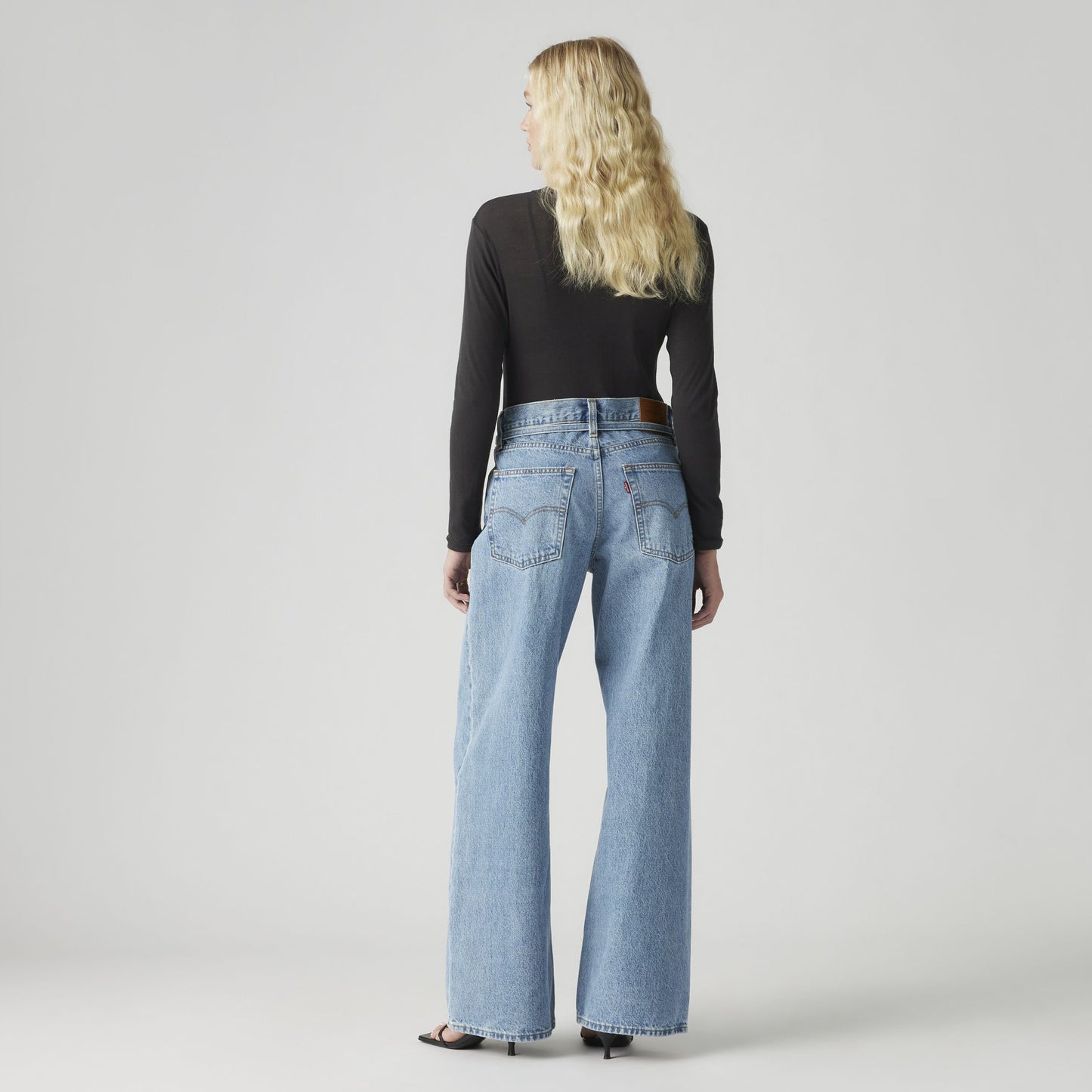 A person with long blonde hair stands away, wearing a black long-sleeve top and Levis' XL Straight, oversized fit, non-stretch denim wide-leg jeans.