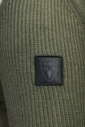 Close-up of Ada Women's Quilted Full Zip Sweater in green knit fabric featuring a black patch with a stylized deer head and "nobis" logo. This Nobis sweater offers warmth with Primaloft Gold Insulation Active+ and remains breathable.