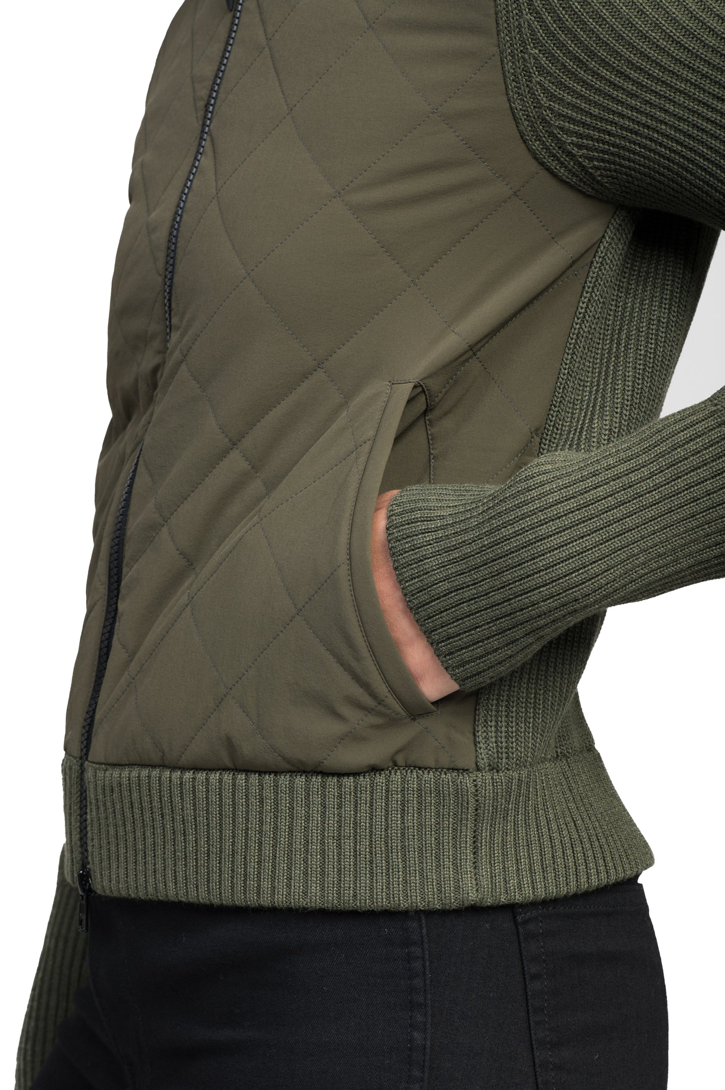 Wearing the Ada Women's Quilted Full Zip Sweater by Nobis, which features ribbed sleeves and Primaloft Gold Insulation Active+ for warmth, a person pairs it with black pants, casually tucking one hand into the pocket.