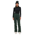 A person in the classic dark green Alessandra Pant by Halfdays, a black long-sleeve shirt, and a beanie stands facing forward against a white background.