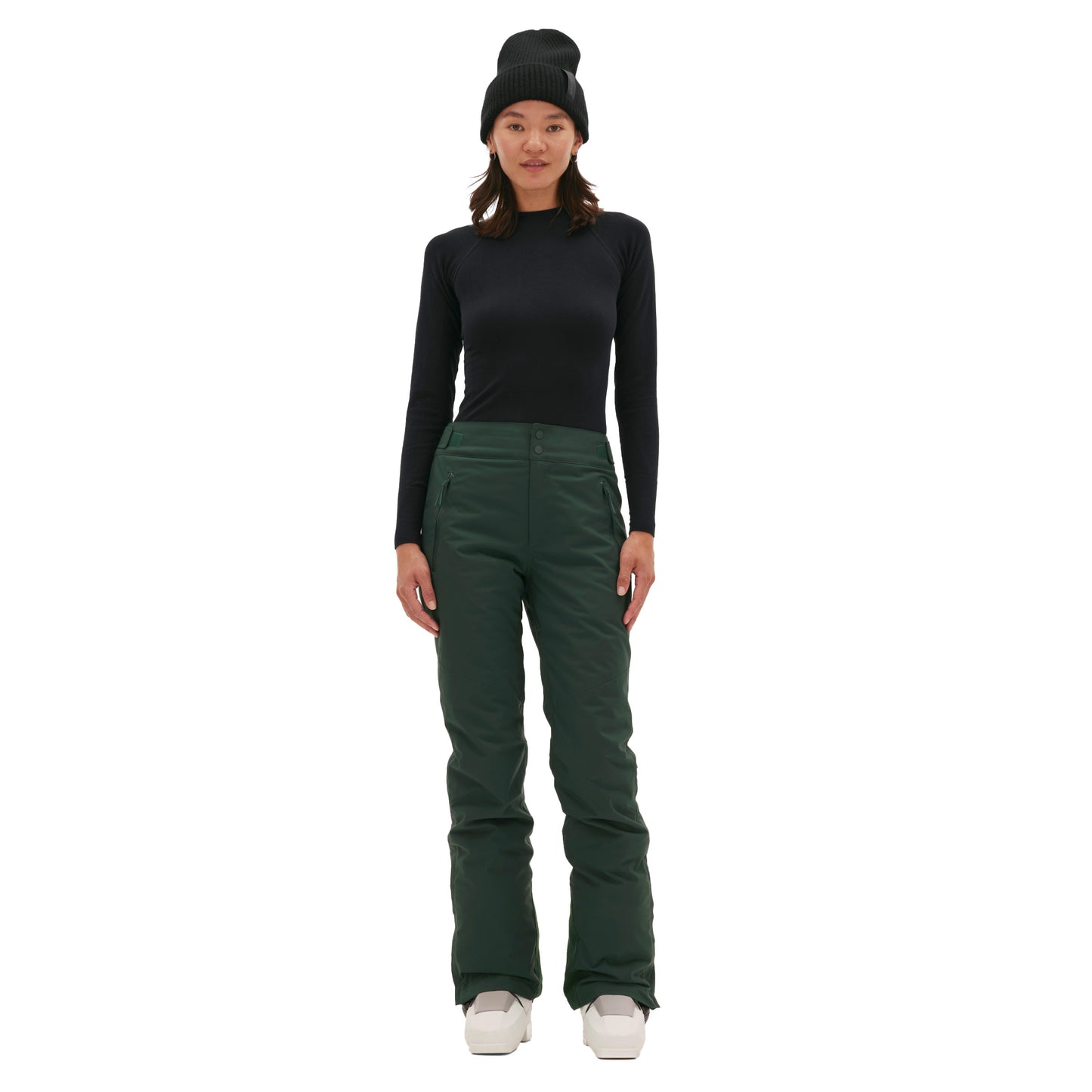 A person in the classic dark green Alessandra Pant by Halfdays, a black long-sleeve shirt, and a beanie stands facing forward against a white background.