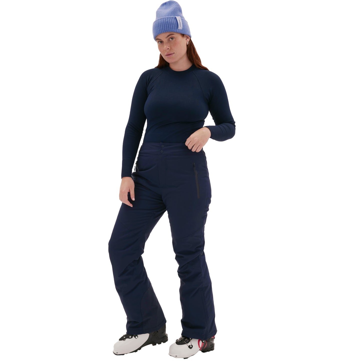 Against a white background, someone stands confidently wearing a light blue beanie, dark long-sleeve top, and Halfdays Alessandra Pant, paired with white boots.