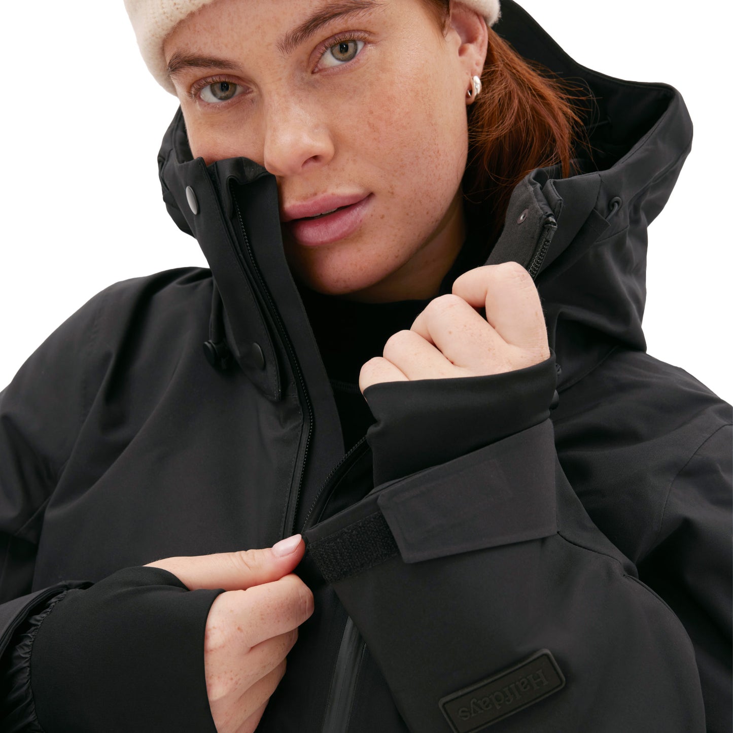 Person wearing a Halfdays Aston Jacket with a white beanie, adjusting the collar and looking at the camera against a mountain backdrop.