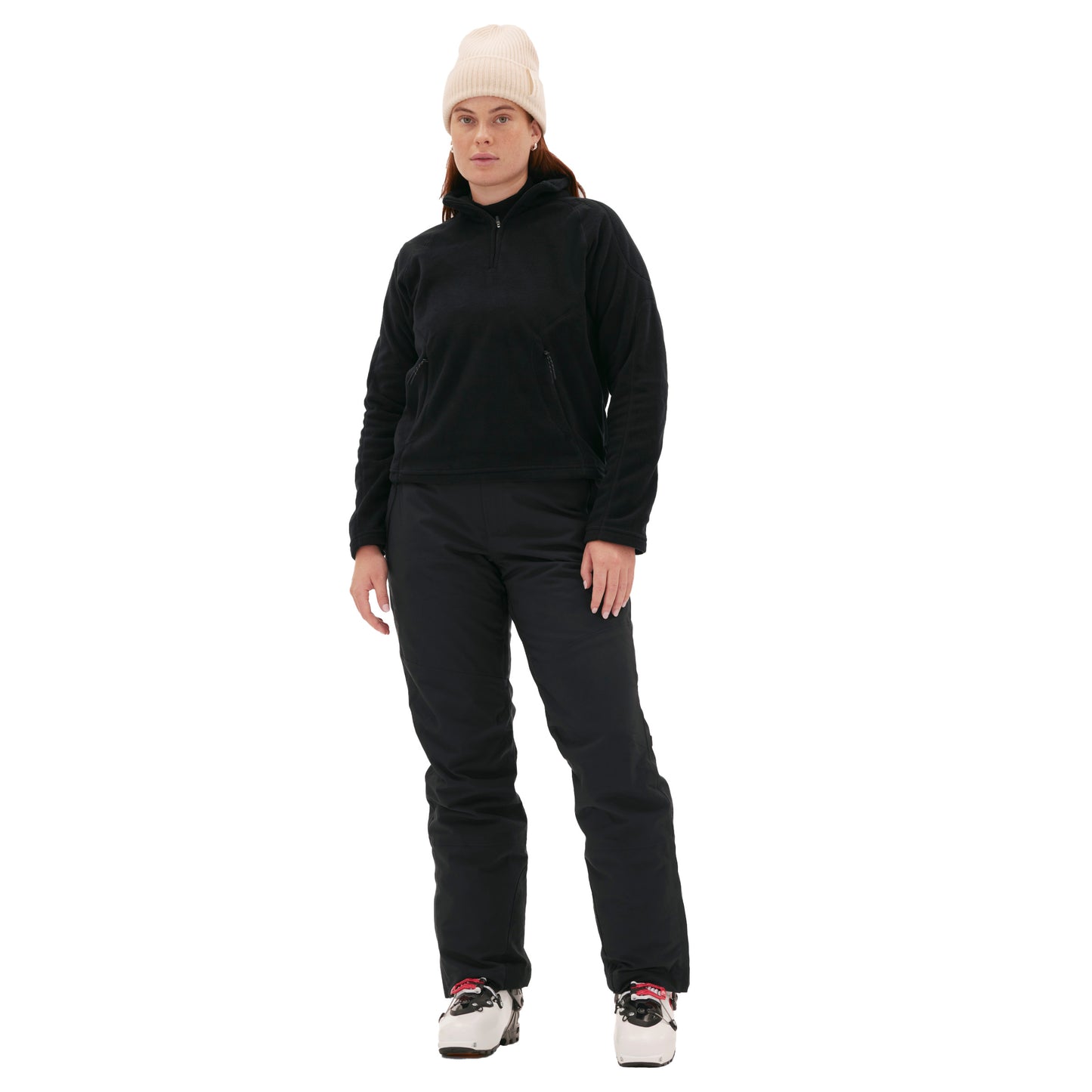 A person wearing a beige beanie, a black Bonnie Fleece Top from Halfdays, black pants, and white sneakers stands against a white background.