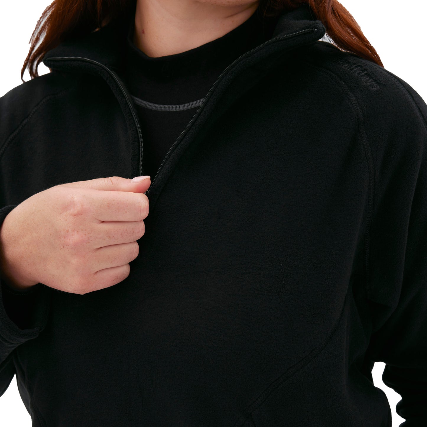 A person wearing a Halfdays Bonnie Fleece Top in black, partially zipped down, reveals a black shirt underneath.