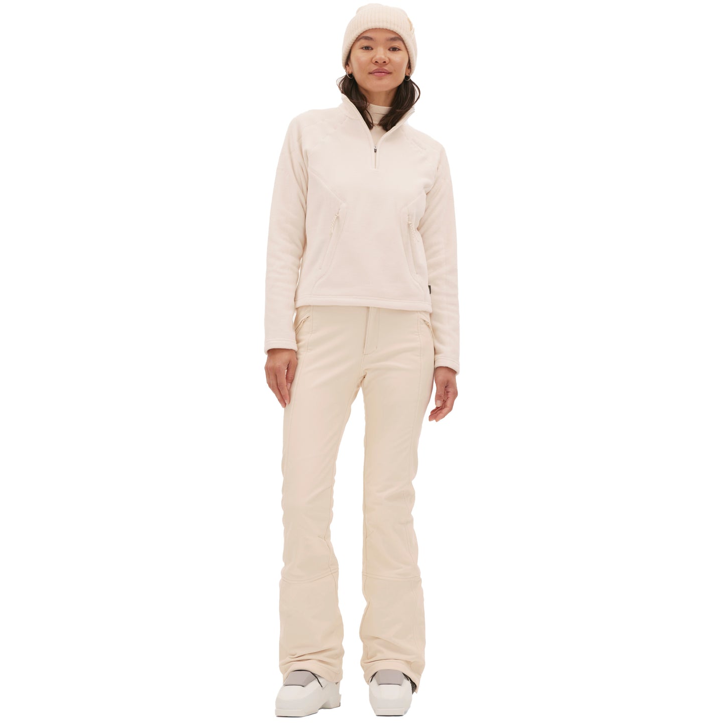 A person wears a light pink winter ensemble that includes the Bonnie Fleece Top by Halfdays and a beanie, paired with boots, standing against a white backdrop.