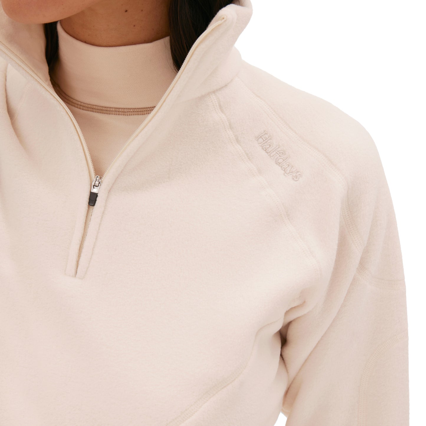 Close-up of a person wearing the Halfdays Bonnie Fleece Top in light beige, featuring a high collar over a matching turtleneck—a perfect performance mid-layer for that high-alpine classic look.