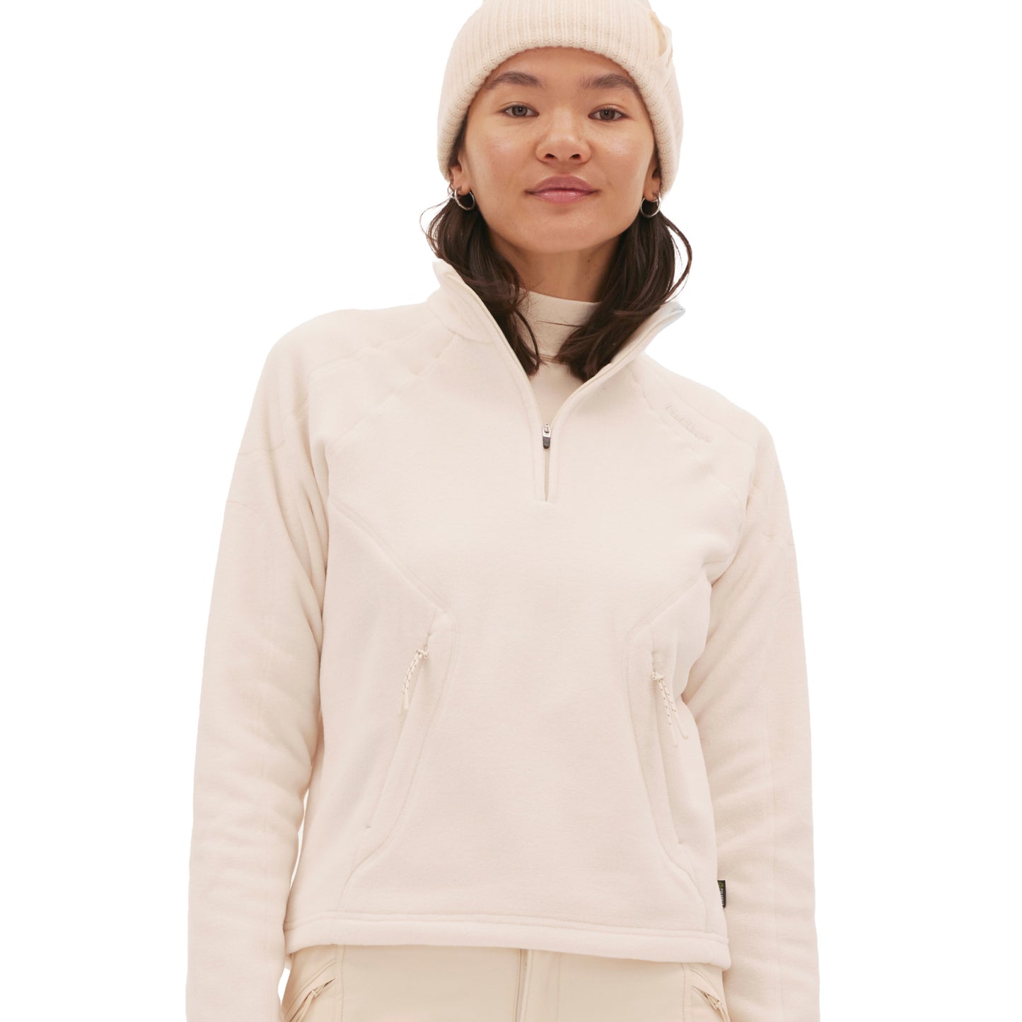 A person wearing a light-colored Bonnie Fleece Top from Halfdays and a beanie stands against a plain white background, embodying the high-alpine classic style.