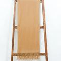 A beige scarf from Alashan, known as The Classic Throw and crafted from luxurious Mongolian cashmere, features fringed ends and is draped over a wooden ladder against a white background.