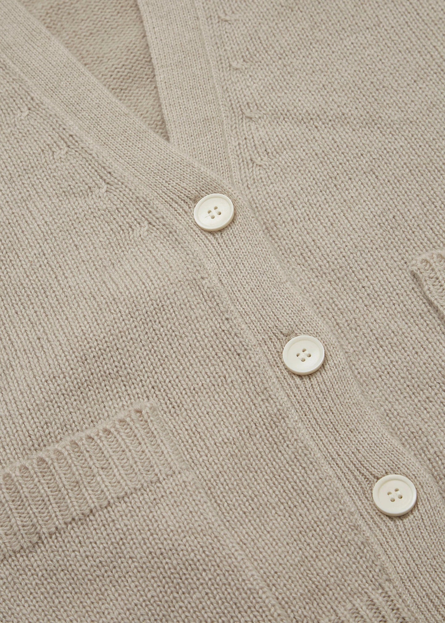 Close-up of the Cora Cardigan by Aiayu, a beige knitted design with white buttons, featuring a V-neck and front pockets.