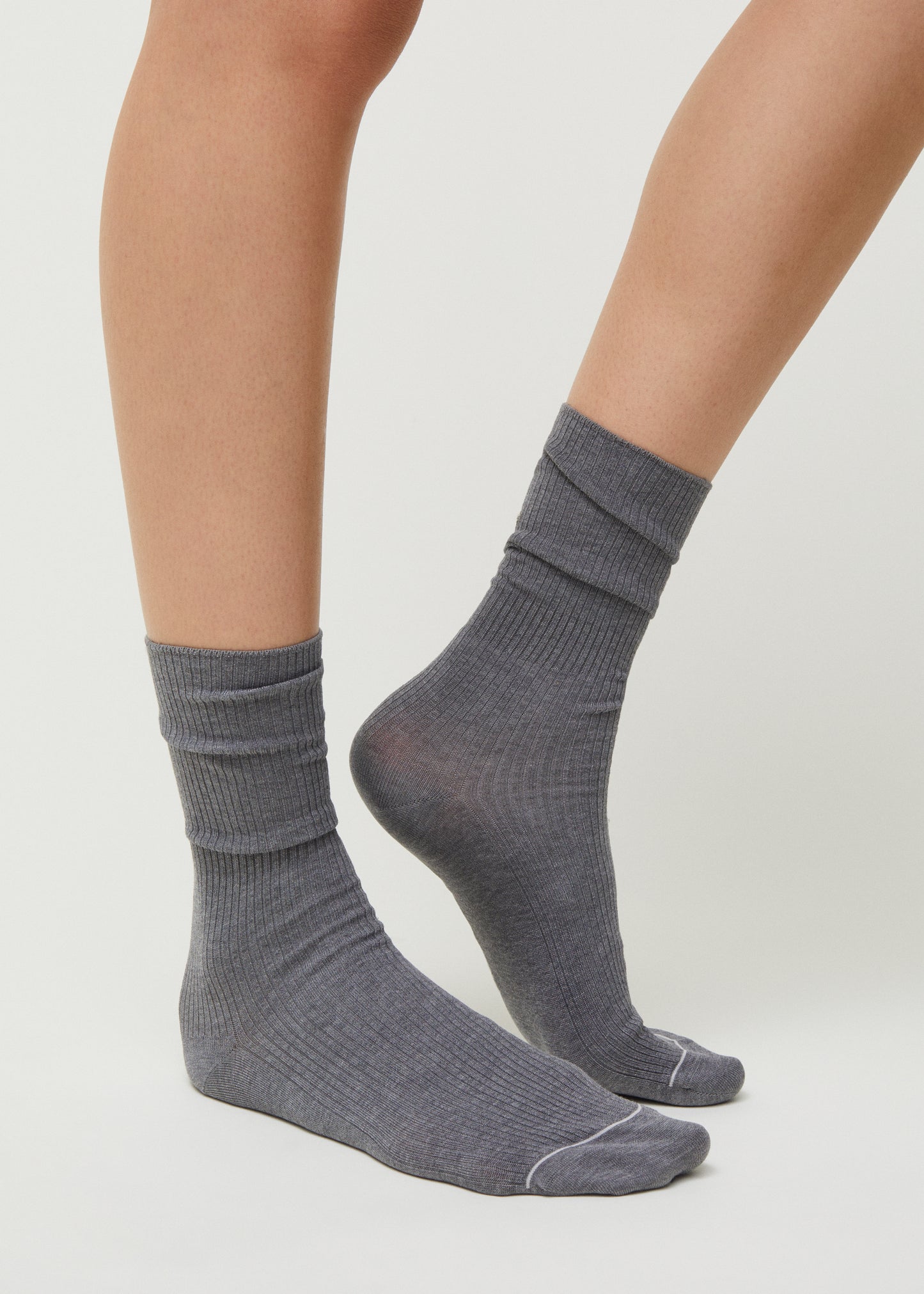 Someone wearing Aiayu's Cotton Rib Socks, GOTS-certified and crafted from organic cotton in gray, stands on a light background.