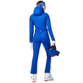 An individual wearing the Goldbergh Coureur Ski Suit in Dazzling Blue is holding a helmet while facing away.