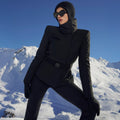 A person dressed in the Elegante Ski Jacket by Goldbergh and sunglasses stands confidently against a backdrop of snowy mountains.