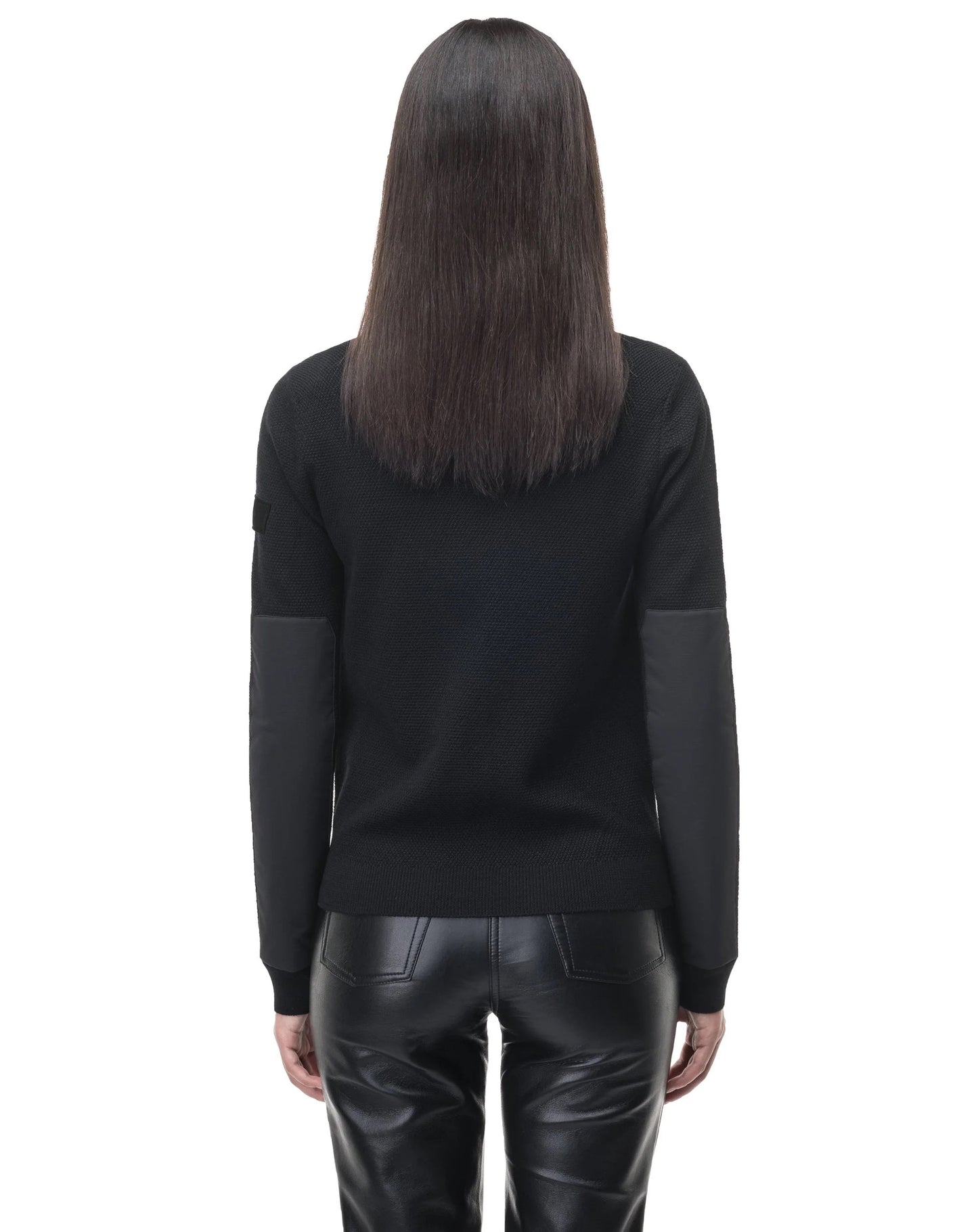 A person with long, straight hair, dressed in the stylish Evo Women's Performance Full Zip Sweater by Nobis and sleek black leather pants featuring subtle Merino wool trimming, is shown from the back against a white background.