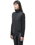 A person wearing the Evo Women's Performance Full Zip Sweater by Nobis, paired with black leather pants, stands against a white background.