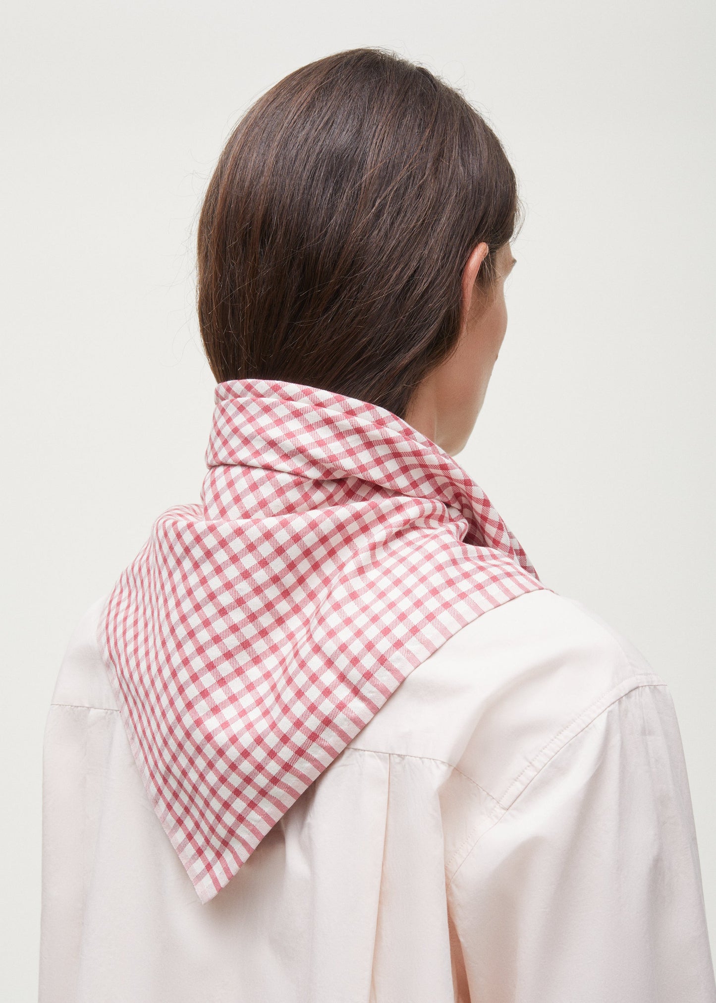 Person with long brown hair wearing a pink and white Familia Scarf by Aiayu and a light-colored shirt, seen from behind.