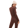 A person dressed in a Fay Merino Top by Halfdays, part of a brown long-sleeve activewear set crafted from merino wool, wearing a white knit beanie and standing sideways.