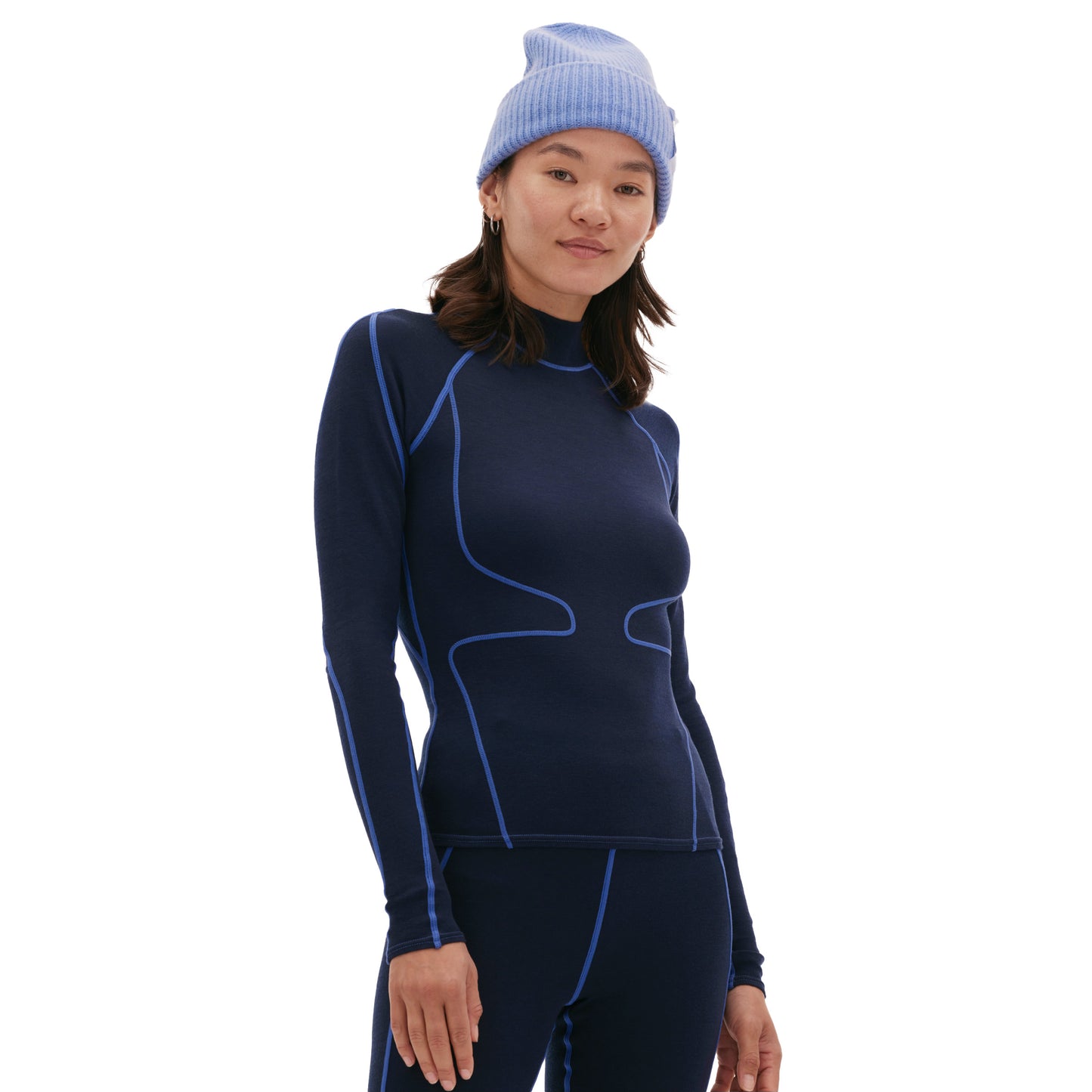 A person is wearing the Fay Merino Top by Halfdays, a cozy blue base layer with matching pants, featuring light blue seam accents and a snug knit beanie.