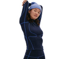 A person dressed in the Fay Merino Top by Halfdays, featuring a navy design with light blue lines and a matching blue beanie, stretches with arms overhead against a white background, showcasing the cozy comfort of their merino wool base layer.