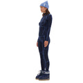 Dressed in a blue ensemble with coordinating hat and boots, the individual stands sideways, poised for the journey ahead, comfortably layered over a Fay Merino Top by Halfdays.