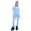 A person dressed in a light blue outfit with a beanie and dark blue boots stands against a white background, showcasing an active outdoor fit with the sleek Johnson top by Halfdays as a seamless nylon base layer underneath.