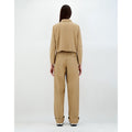 Back view of a person with long hair wearing a beige outfit from the Spring Summer 2024 collection, consisting of a W Scuba Short Jacket Patch Pockets, Camel by Herno and loose-fitting pants made from Sensitive® Fabrics, against a plain backdrop.