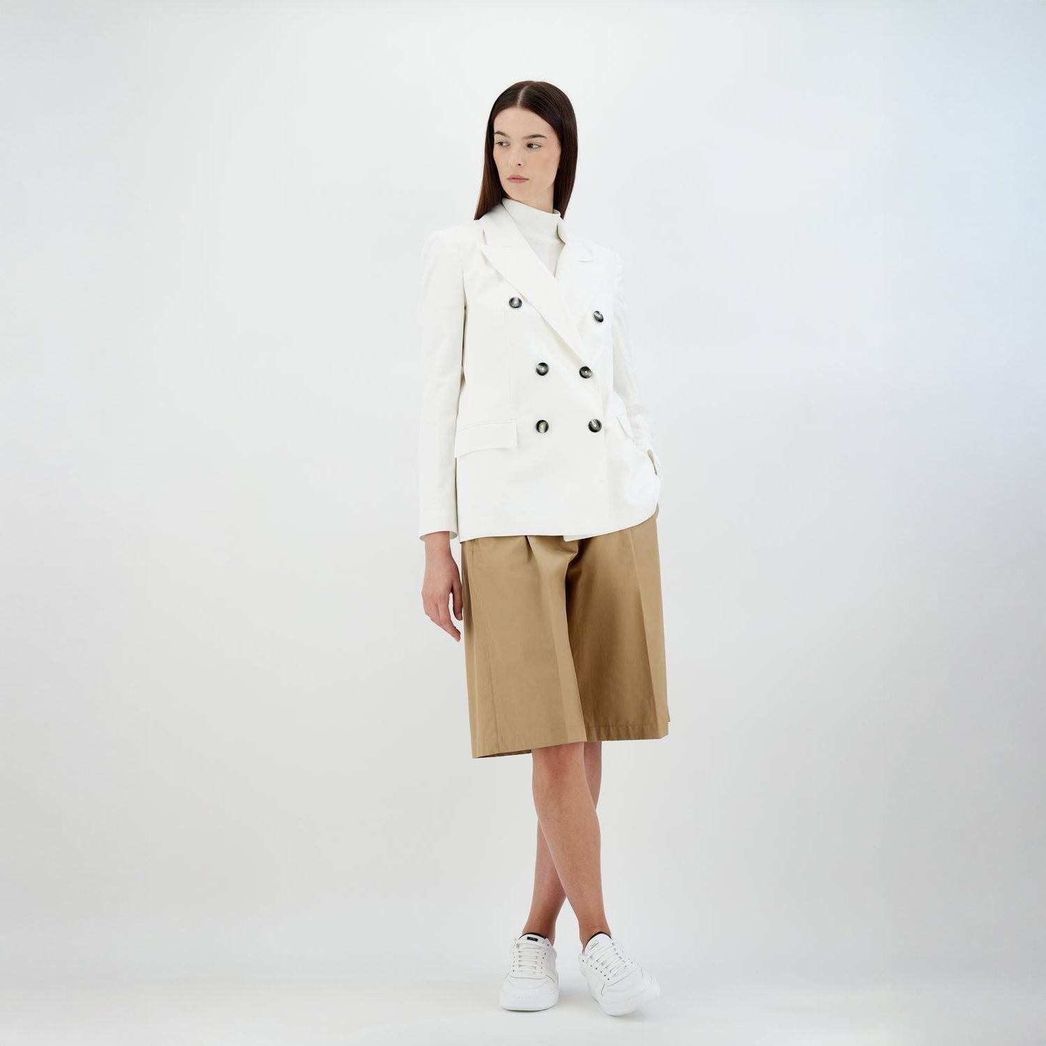 A woman in a Herno "W Light Linen DB Blazer, Bianco" with a feminine fit stands against a plain background, paired with tan wide shorts and white sneakers.