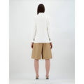 A person with long hair stands facing away, wearing an Herno W Light Linen DB Blazer, Bianco paired with beige knee-length shorts and white sneakers against a plain background.