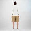 A person with their back to the camera models Herno's W Light Linen DB Blazer in Bianco over tan knee-length shorts and sneakers against a plain backdrop.