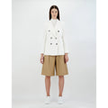 A person stands against a plain background wearing the Herno W Light Linen DB Blazer, Bianco crafted from a linen-cotton blend, beige knee-length shorts, and white sneakers.