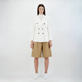 A person stands against a plain background wearing Herno's W Light Linen DB Blazer in Bianco, paired with beige knee-length shorts and white sneakers.