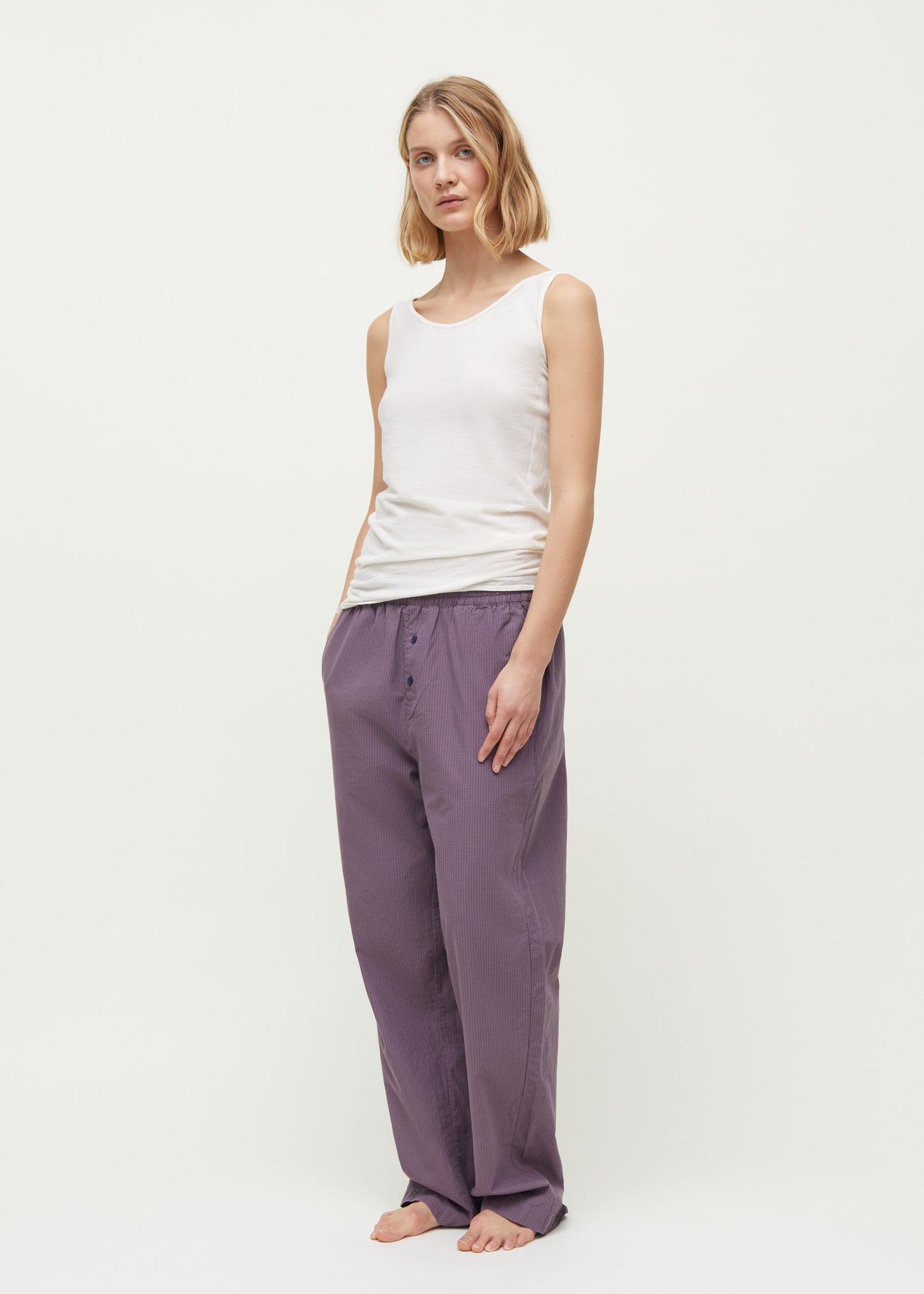 A person in a Gentle Tank by Aiayu, a luxury tank top made of cotton cashmere blend, paired with loose purple pants stands barefoot against a plain background.