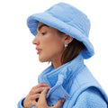 A person wearing a slalom-quilted, light blue puffer jacket and the Golden Bucket Hat from Halfdays glances to the side.