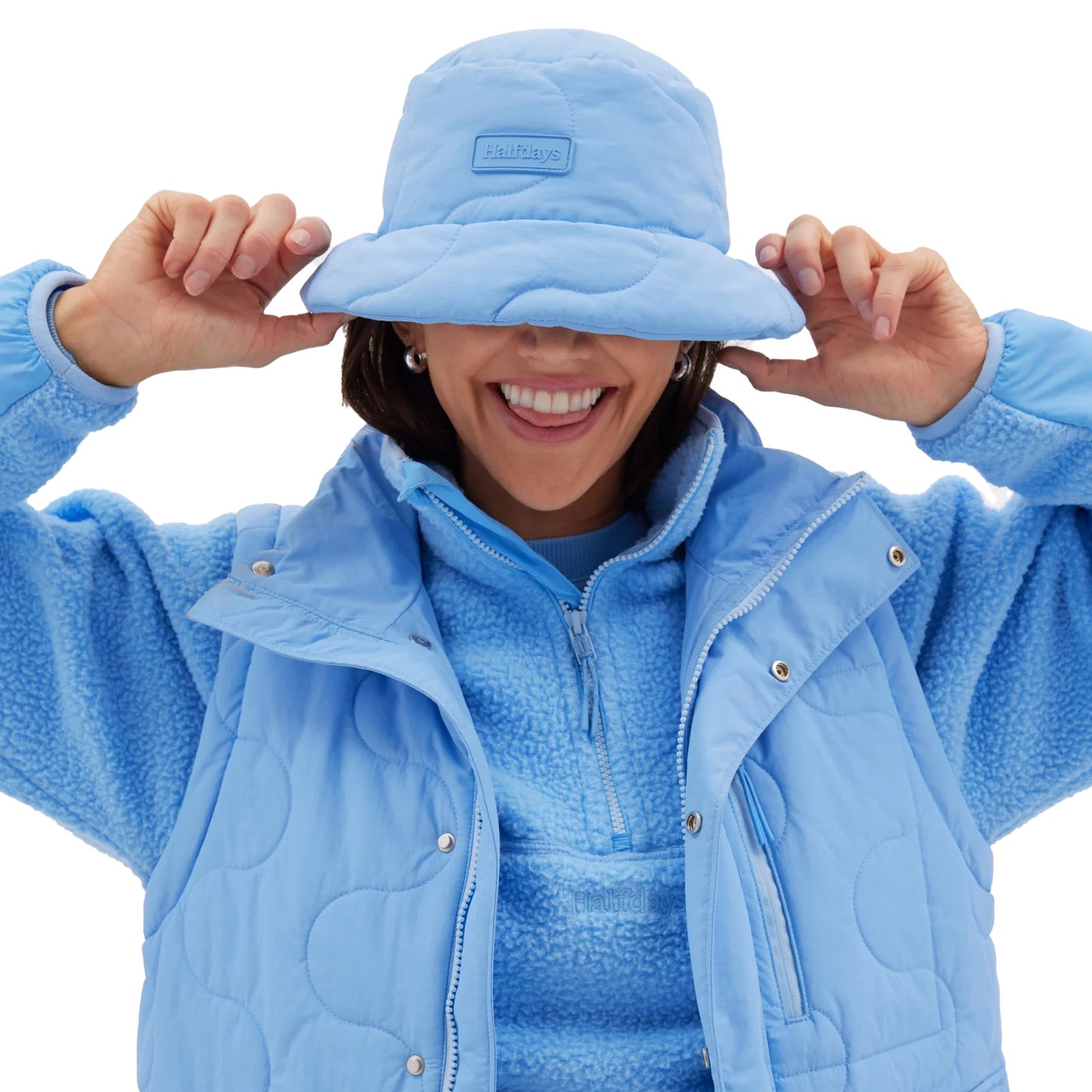 A smiling person wears a blue slalom-quilted fleece outfit and the matching Halfdays Golden Bucket Hat, ready for trail hikes.