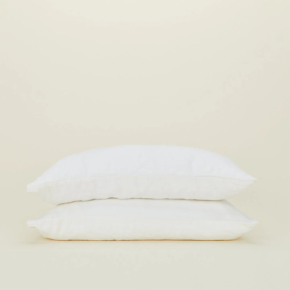 Two white pillows stack elegantly against a plain beige background, dressed in Hawkins New York's Standard Linen Pillow Case.