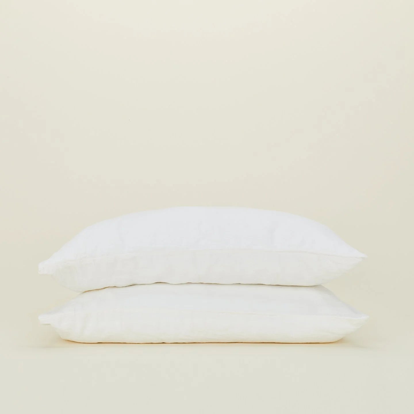 Two white pillows stack elegantly against a plain beige background, dressed in Hawkins New York's Standard Linen Pillow Case.