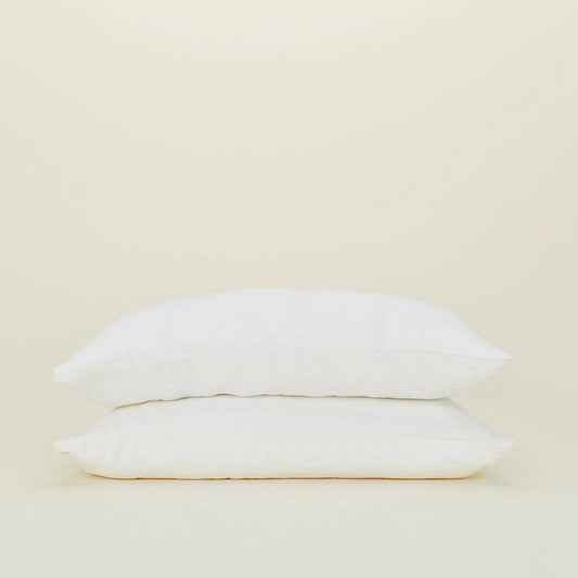 Two white pillows stack elegantly against a plain beige background, dressed in Hawkins New York's Standard Linen Pillow Case.