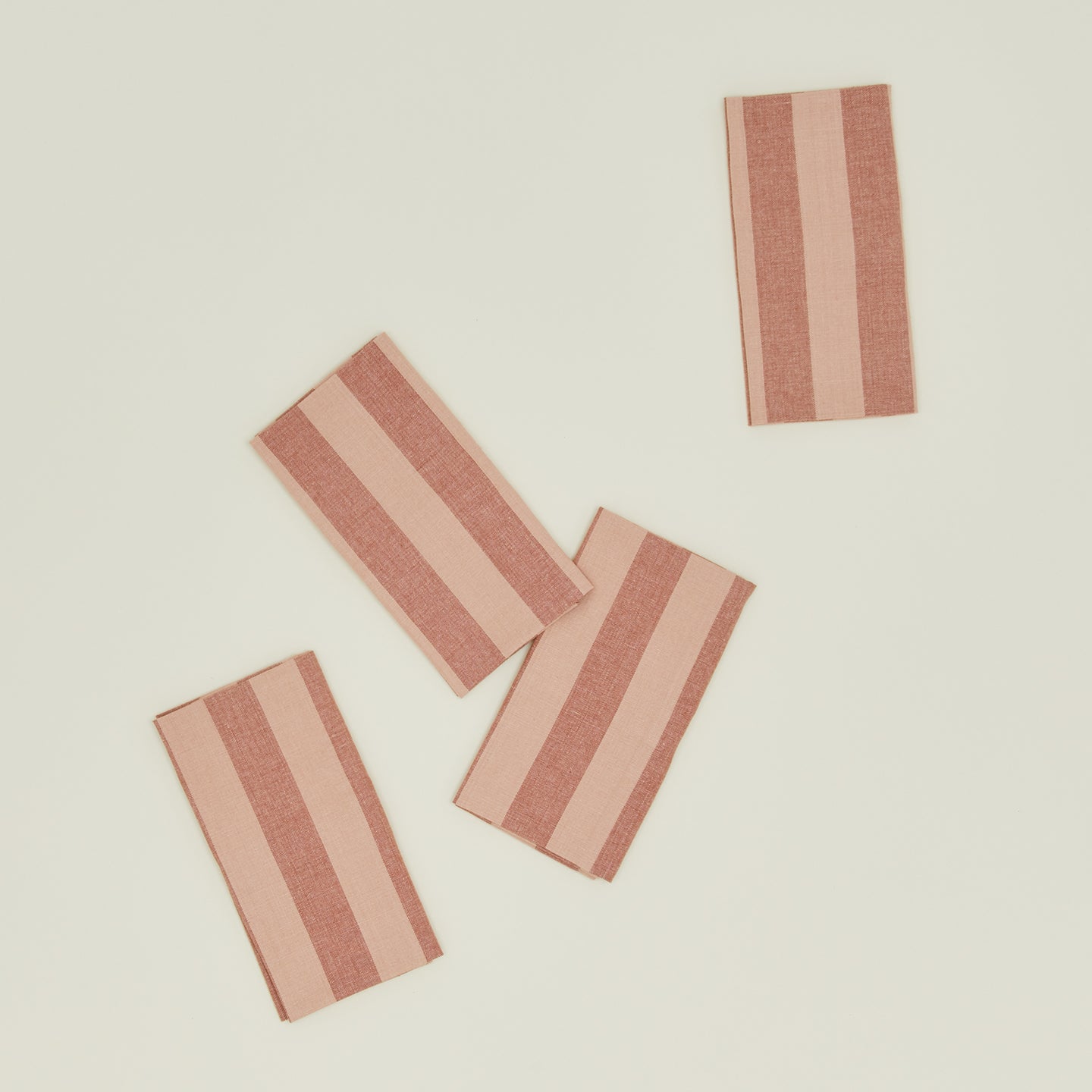 The Essential Striped Dinner Napkins by Hawkins New York feature four pieces with alternating light and dark pink stripes on a light beige background, embodying the relaxed style of our Essential Collection.