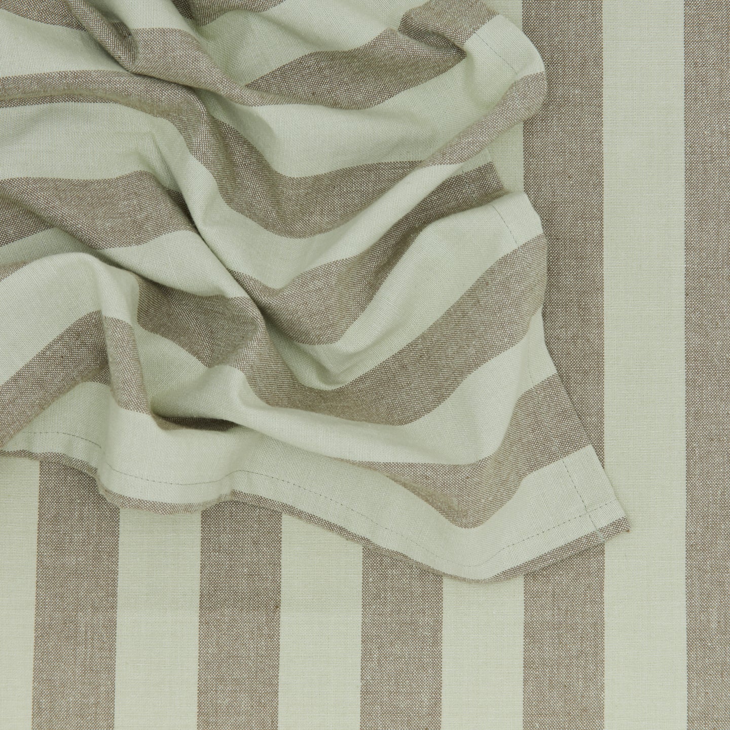 A close-up of the Essential Striped Dinner Napkins by Hawkins New York showcases a folded section with wide beige and sage green stripes, ideal for creating relaxed pieces to complement your home basics.