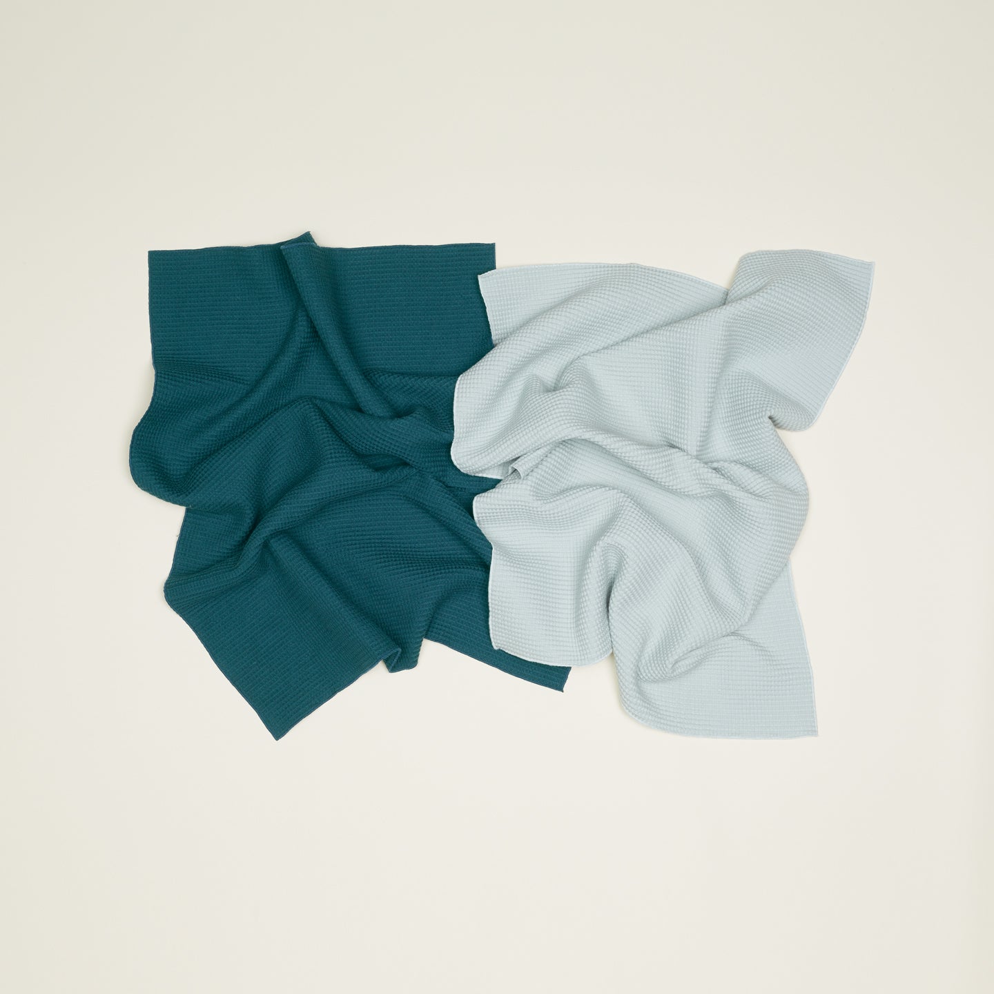 The Essential Waffle Dish Towel set from Hawkins New York features dark green and light gray fabrics with a waffle weave, laid flat on a light background. Soft folds suggest their super absorbent and quick-drying nature.