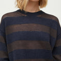 A person wearing the Aiayu Haldis Wool Sweater in dark blue and brown, featuring a striped knit design with a loose weave pattern that showcases the charm of textured knitwear.