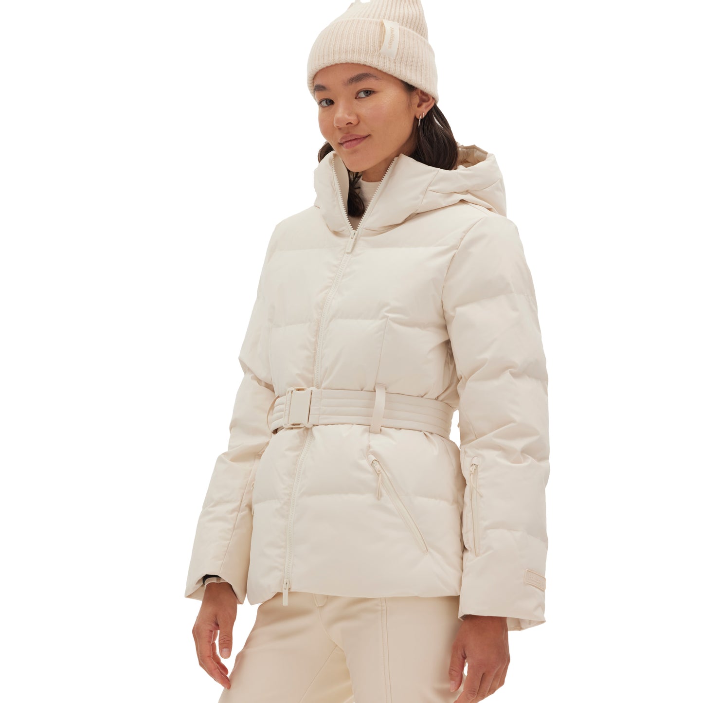 A person wearing the Hedy Puffer Jacket by Halfdays and a beanie, designed with mountain performance features, is standing against a white background.