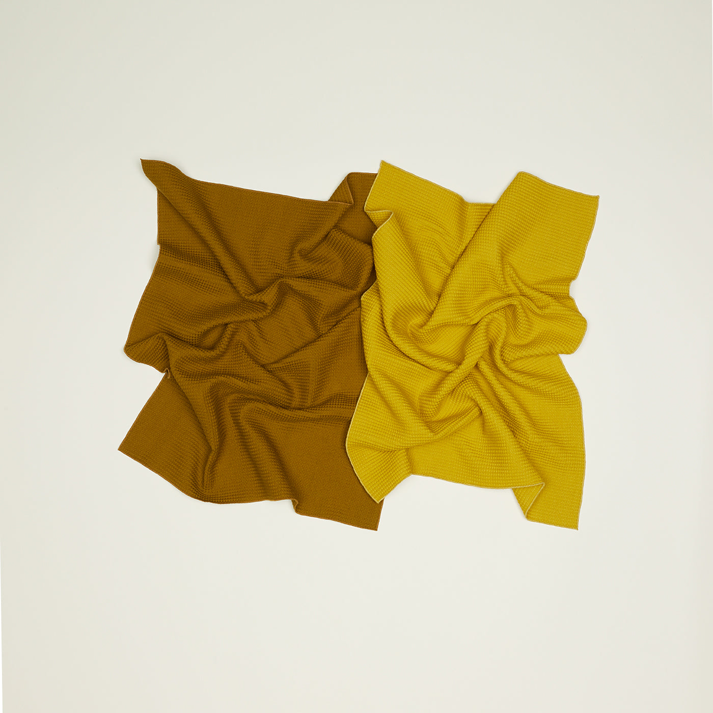 A set of two Essential Waffle Dish Towels from Hawkins New York, featuring one towel in dark mustard and the other in light yellow, are arranged on a light backdrop. These textured towels are not only stylish but also super absorbent and quick to dry.