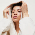 A person is posing against a plain background, adjusting the hood of an Aiayu Hooded Terry Bathrobe, made from Organic Chetna Cotton.