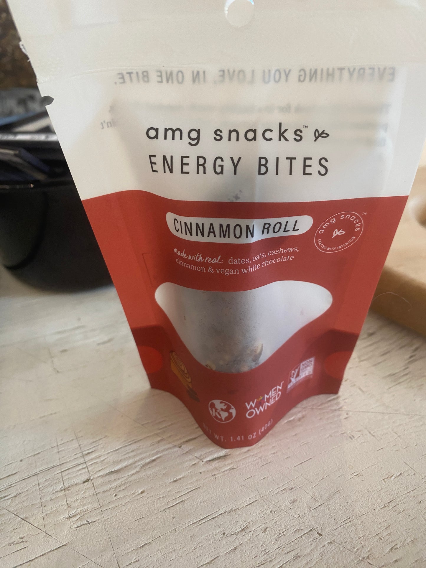 A package of "Energy bites cinnamon roll - amg snacks" from the brand Westerlind sits on a table. The label indicates the snack is made with dates, oats, cashews, cinnamon, and vegan white chocolate.