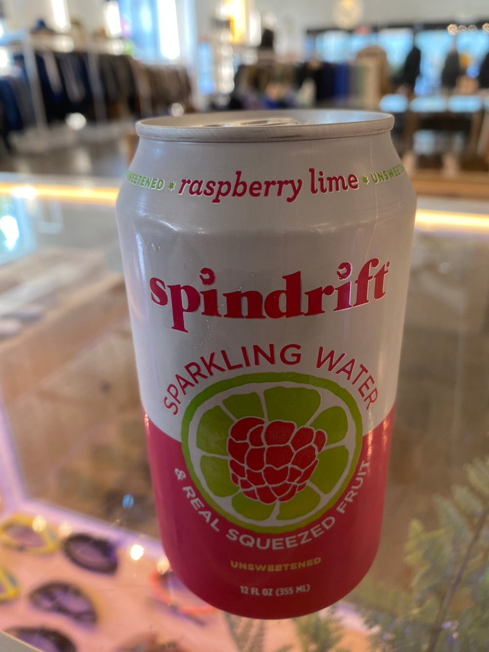 A can of Westerlind Raspberry Lime Spindrift perched on a glass table. The label states "Sparkling Water & Real Squeezed Fruit," and the can holds 12 fl oz (355 ml).